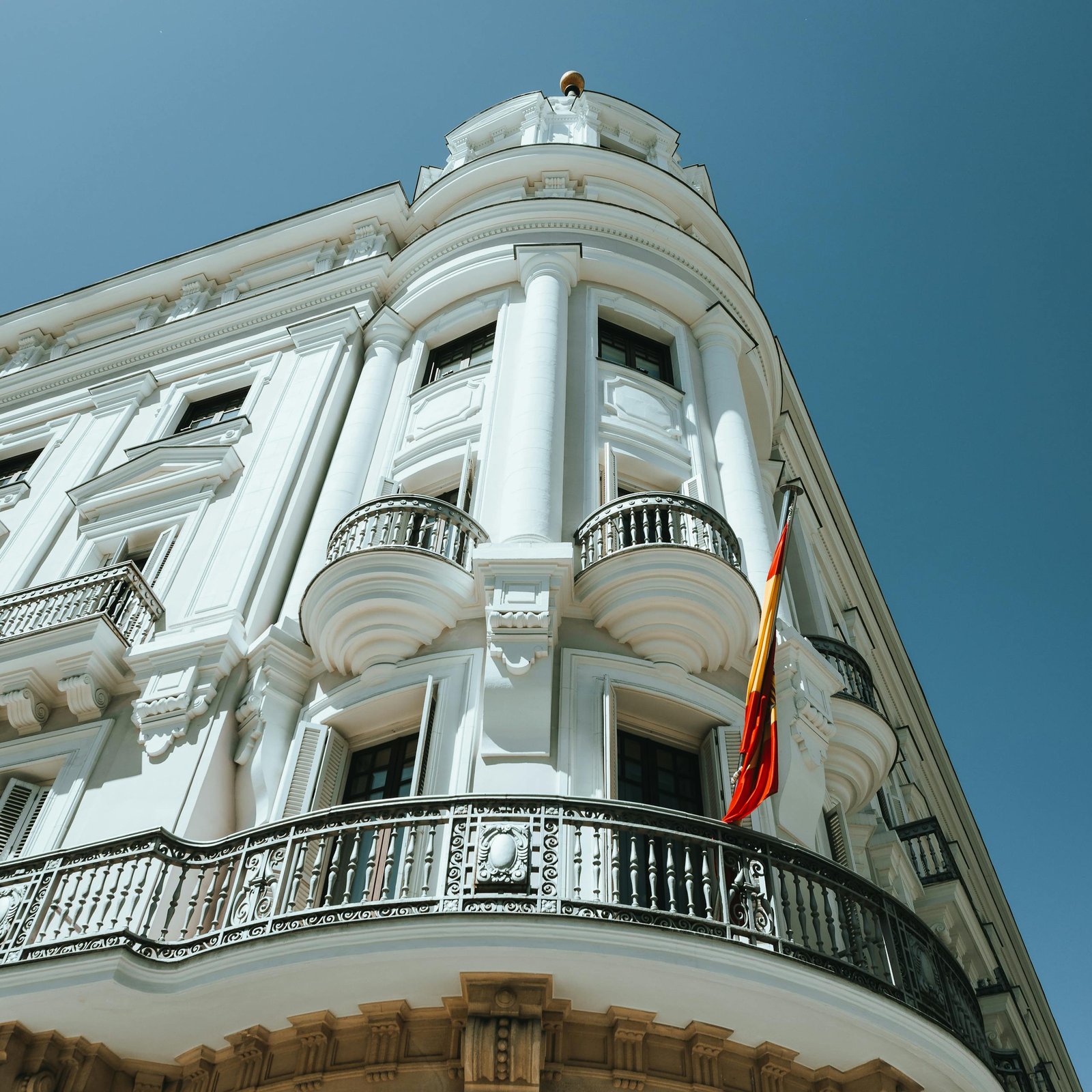 Stunning white building with Spanish flag under a clear blue sky, showcasing classic architectural design.
